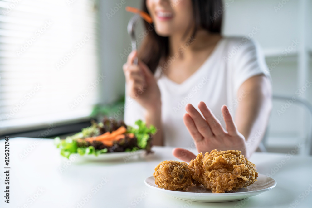 Woman on dieting for good health concept, young women use hands to push fried chicken and choose to eat vegetables for good health. - obrazy, fototapety, plakaty 