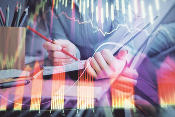 A woman hands writing information about stock market in notepad. Forex chart holograms in front. Concept of research. Multi exposure