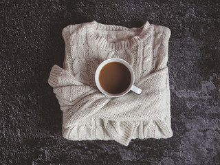 Canvas Print - Cream chunky knitted sweater with cup of coffee or tea isolated on dark textured background. Flat lay. Top view.