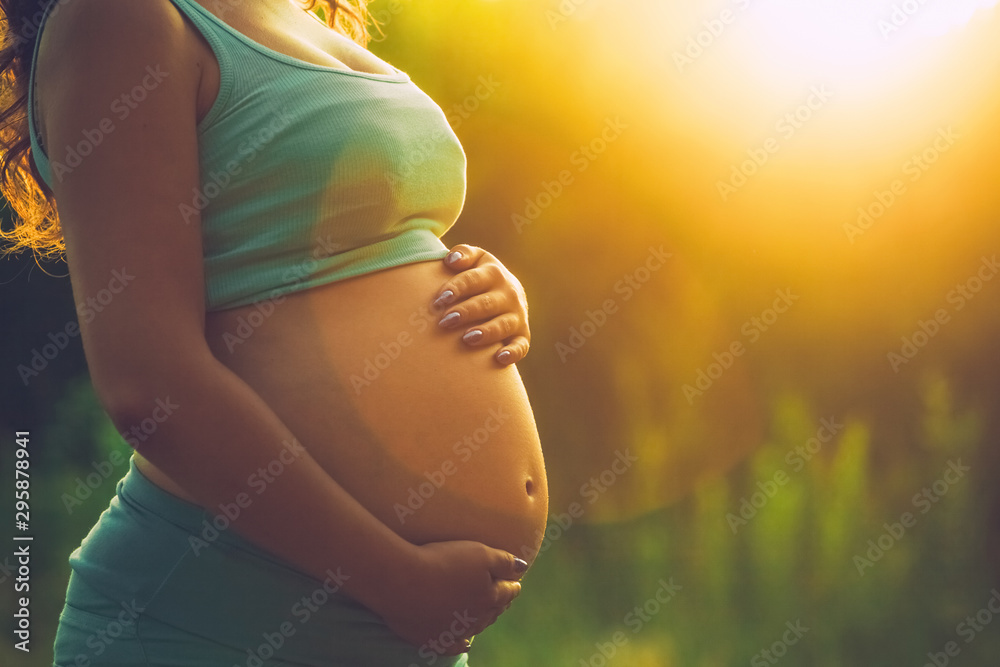 Adult pregnant woman on against the backdrop of the sunset in the park. 9 months of pregnancy and childbirth. - obrazy, fototapety, plakaty 