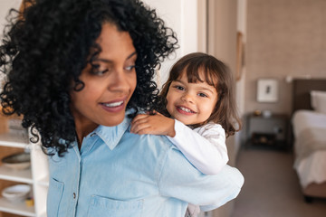 Wall Mural - Cute little girl getting a piggyback from her smiling mom