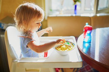 Wall Mural - Adorable little girl eating pasta at home