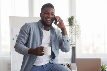 Cheerful entrepreneur talking on phone and drinking coffee in office