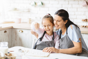 Wall Mural - Pretty little girl and her attractive mom making cookies together