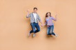 © deagreez - Hi there. Full length photo of two people lady guy jumping high holding hands showing v-sign symbols wear casual plaid jeans clothes isolated beige color background