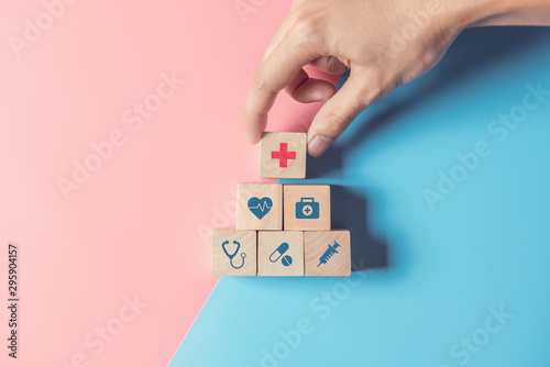 Fotomural Health Insurance Concept, Hand of man arranging wood cube stacking with icon healthcare medical on pastel blue and pink background, copy space