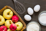 Fototapeta Kuchnia - Top view of apples, eggs, sugar, flour and whisk on wooden background