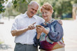 © Leika production - Old man and old woman are using together one phone and smiling while walking in a park on a warm day