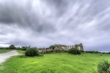 Wide Shot Of Abandoned Building Ruins In A Green Field Under The Dark Cloudy Sky