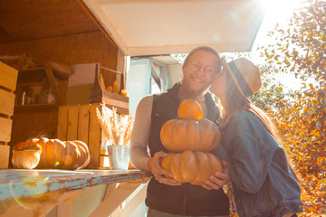 Young adult woman and man kissing and buying fresh pumpkin in grocery shop