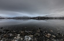 Beautiful Shot Of Rocks On The Body Of Water Surrounded By Fjord Under A Gray Cloudy Sky