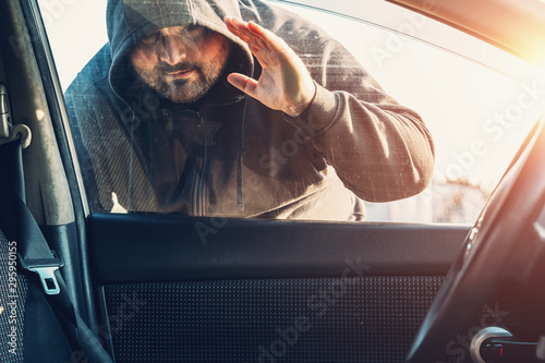 Fotografía Criminal person in hood looks inside car through glass or window, Robber or car
