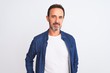 © Krakenimages.com - Middle age handsome man wearing blue denim shirt standing over isolated white background Relaxed with serious expression on face. Simple and natural looking at the camera.