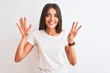 © Krakenimages.com - Young beautiful woman wearing casual t-shirt standing over isolated white background showing and pointing up with fingers number eight while smiling confident and happy.