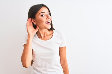 Wall Mural - Young beautiful woman wearing casual t-shirt standing over isolated white background smiling with hand over ear listening an hearing to rumor or gossip. Deafness concept.