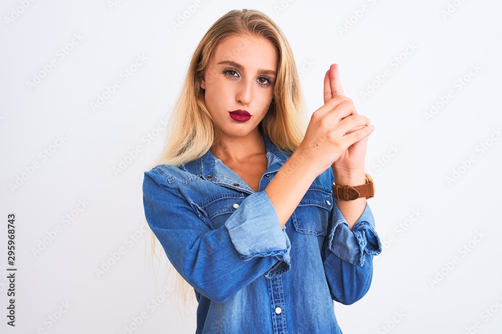 Young beautiful woman wearing casual denim shirt standing over isolated white background Holding symbolic gun with hand gesture, playing killing shooting weapons, angry face