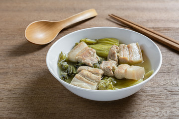 close up of pickled mustard green soup with pork belly in a bowl on wooden table. asian homemade style food concept.