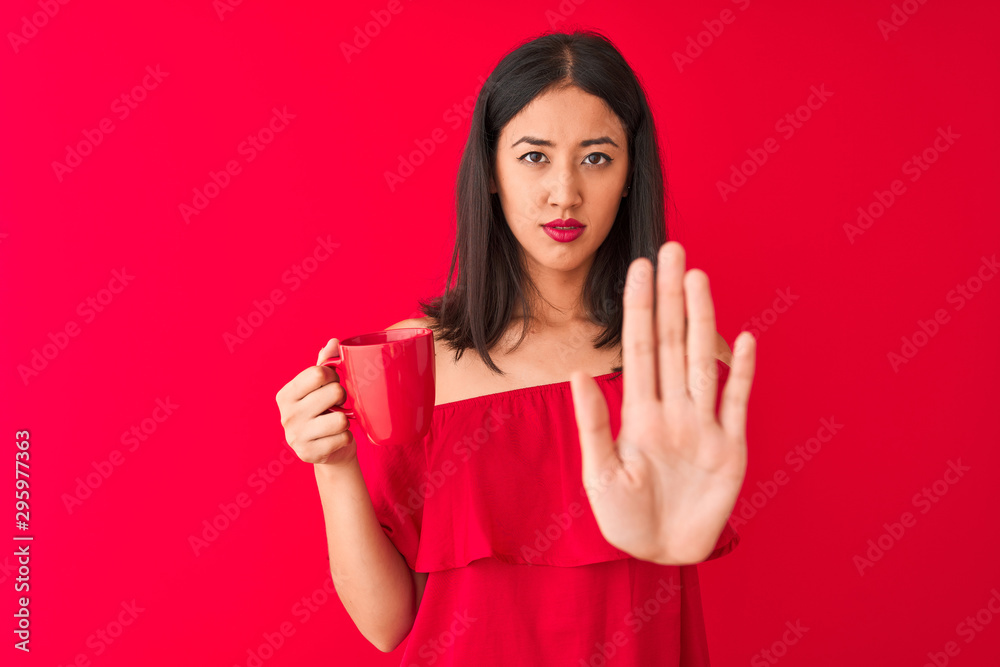 Young beautiful chinese woman drinking cup of coffee standing over isolated red background with open hand doing stop sign with serious and confident expression, defense gesture - obrazy, fototapety, plakaty 