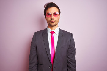 Sticker - Young handsome businessman wearing suit and sunglasses over isolated pink background with serious expression on face. Simple and natural looking at the camera.