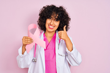 Sticker - Young arab doctor woman with curly hair holding cancer ribbon over isolated pink background happy with big smile doing ok sign, thumb up with fingers, excellent sign