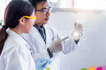 Canvas Print - Attractive scientist looking sample with microscope at laboratory with lab glassware background. Science or chemistry research and development concept.