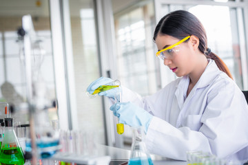 Canvas Print - Attractive scientist woman looking chemical sample in flask at laboratory with lab glassware background. Science or chemistry research and development concept.