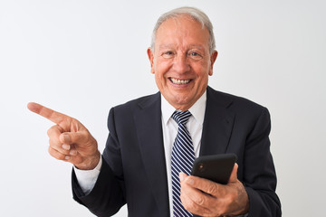 Senior grey-haired businessman using smartphone standing over isolated white background very happy pointing with hand and finger to the side