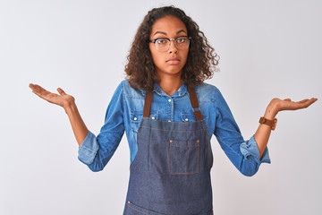 Wall Mural - Young brazilian chef woman wearing apron and glasses over isolated white background clueless and confused expression with arms and hands raised. Doubt concept.