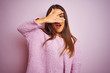 Young beautiful woman wearing casual sweater standing over isolated pink background peeking in shock covering face and eyes with hand, looking through fingers with embarrassed expression.
