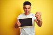 © Krakenimages.com - Young brazilian man holding blackboard standing over isolated yellow background annoyed and frustrated shouting with anger, crazy and yelling with raised hand, anger concept
