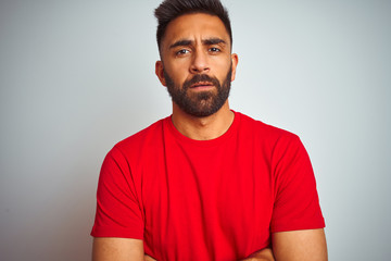 Wall Mural - Young indian man wearing red t-shirt over isolated white background skeptic and nervous, disapproving expression on face with crossed arms. Negative person.