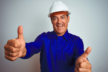 Wall Mural - Handsome middle age worker man wearing uniform and helmet over isolated white background approving doing positive gesture with hand, thumbs up smiling and happy for success. Winner gesture.