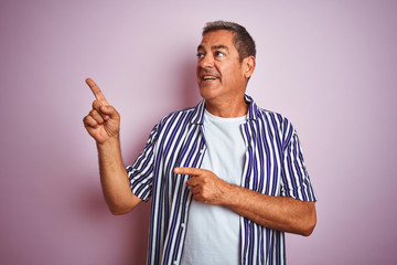 Wall Mural - Handsome middle age man wearing striped shirt standing over isolated pink background smiling and looking at the camera pointing with two hands and fingers to the side.