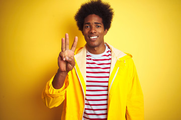 Sticker - African american man with afro hair wearing rain coat standing over isolated yellow background showing and pointing up with fingers number three while smiling confident and happy.