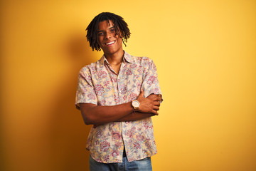 Afro man with dreadlocks on vacation wearing floral shirt over isolated yellow background happy face smiling with crossed arms looking at the camera. Positive person.