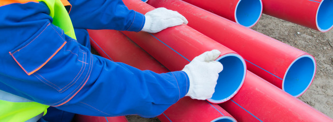 Wall Mural - worker’s hands, in white gloves, against a background of red plastic pipes stacked on top of each other, close-up