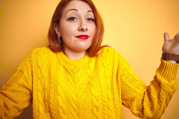 Poster - Young redhead woman wearing winter sweater standing over isolated yellow background clueless and confused expression with arms and hands raised. Doubt concept.