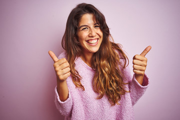 Young beautiful woman wearing sweater standing over pink isolated background success sign doing positive gesture with hand, thumbs up smiling and happy. Cheerful expression and winner gesture.