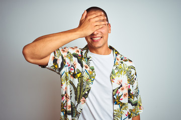 Poster - Young handsome man on holidays wearing Hawaiian shirt over white background smiling and laughing with hand on face covering eyes for surprise. Blind concept.