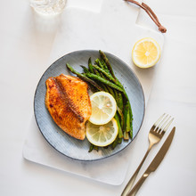 Roasted Tilapia Fish With Asparagus On A White Marble Tray. Healthy Mediterranean Diet Lunch Or Dinner. Top View, Flat Lay.