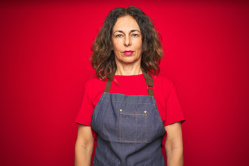 Sticker - Middle age senior woman wearing apron uniform over red isolated background Relaxed with serious expression on face. Simple and natural looking at the camera.