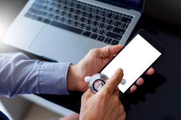 Mockup male doctor hand holding stethoscope and using mobile smart phone with blank white screen, work on computer notebook on dark table background. Top view. Telemedicine , teleconference concept.