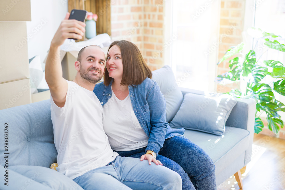 Young couple sitting on the sofa at new home taking a selfie photo ...