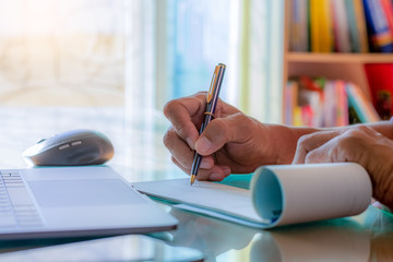 Business man hand writing and signing cheque book with laptop computer on the wooden table at modern home office.