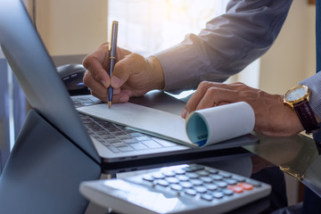 Business man hand writing and signing cheque book with laptop computer on the wooden table at modern home office.	