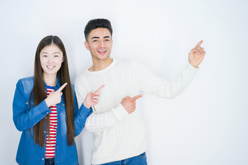 Sticker - Beautiful young asian couple over white isolated background smiling and looking at the camera pointing with two hands and fingers to the side.