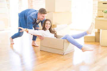 Poster - Beautiful young couple smiling in love having fun riding inside a cardboard box, celebrating moving to a new home