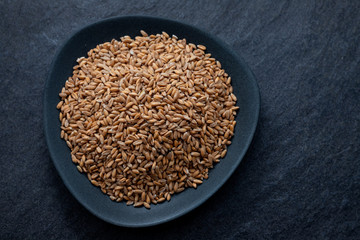 Sticker - uncooked spelt on black dish on ceramic background