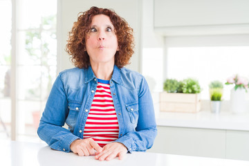 Poster - Middle age senior woman with curly hair wearing denim jacket at home making fish face with lips, crazy and comical gesture. Funny expression.