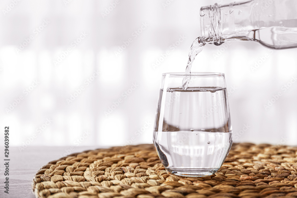Pouring of fresh water from bottle into glass on table